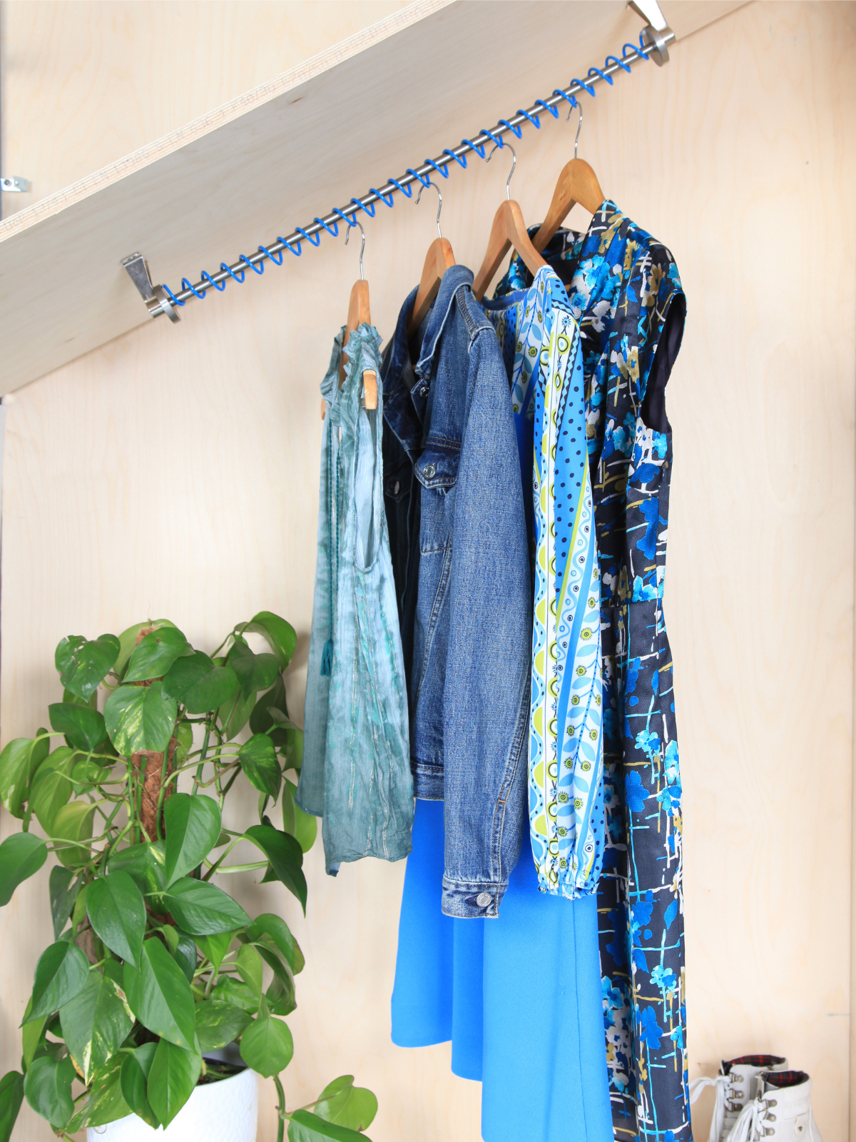 Internals of slanted ceiling wardrobe with Zebedee Blue angled clothes rail mounted into a wooden wardrobe and clothes hangers and full length clothes