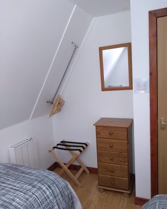 Very steeply angled sloped roof with a clothing rail fitted. Clothes hangers are hanging from the railing.