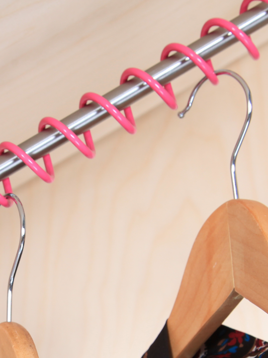 A close up of Zebedee Hanging Rail powder coated in pink with wooden coat hangers