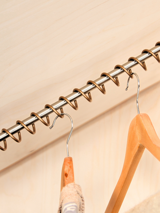 Antique bronze Zebedee clothes rail with clothes hangers hanging on it, set in an under eaves alcove against a wooden background.