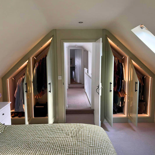 Attic bedroom with sloped ceiling fitted wardrobes, doors open revealing Zebedee's space saving sloped ceiling clothes rails, illuminated by recessed lights.