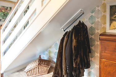 Understairs with coats hanging on an angled top fixed clothes rack, wooden dresser, and decorative elements.