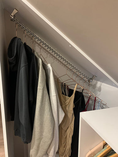 Clothing hanging on a top fixed sloping clothes rail  in a modern under eaves closet