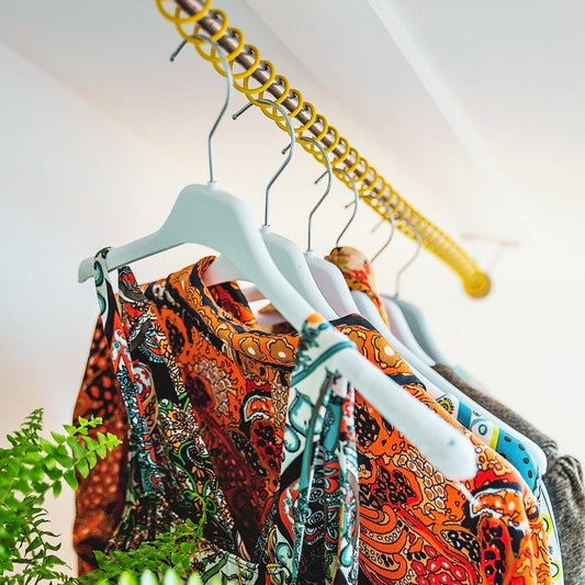 Colorful patterned shirts on clothes hanging with a ceiling mounted Zebedee Yellow sloping clothes rail against a white wall