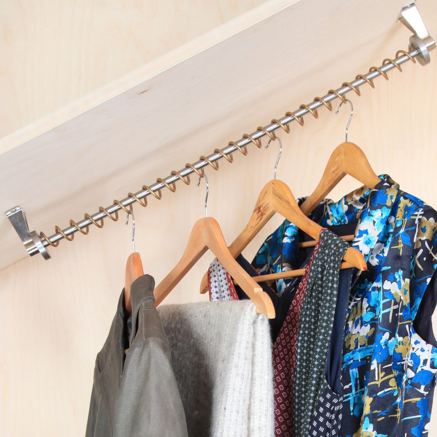 Clothing items hanging on angled clothes rail with wooden hangers against a sloped ceiling neutral wall.