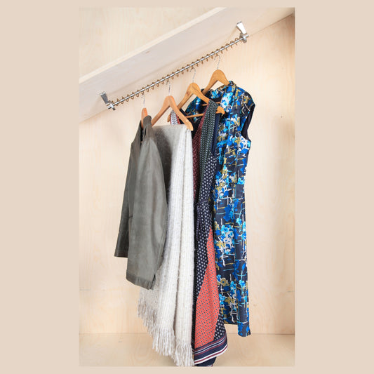 Clothing items hanging on an angled clothes rail against a plain wall, set into a under eaves alcove