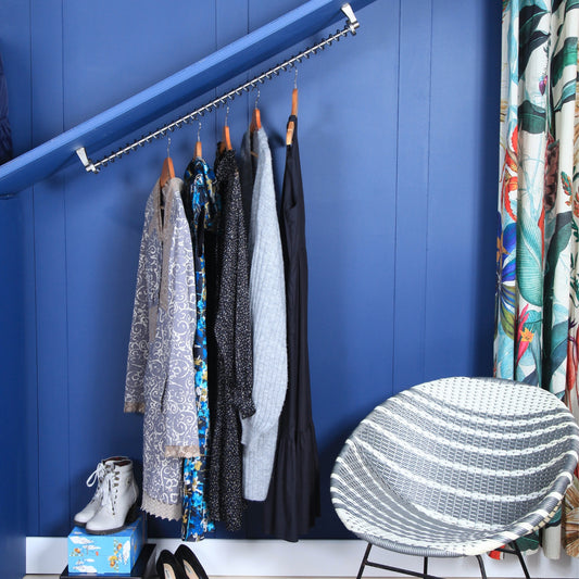 Clothing hanging on a sloping hanging rail, under angled eaves against a blue wall with a chair and shoes in the foreground.
