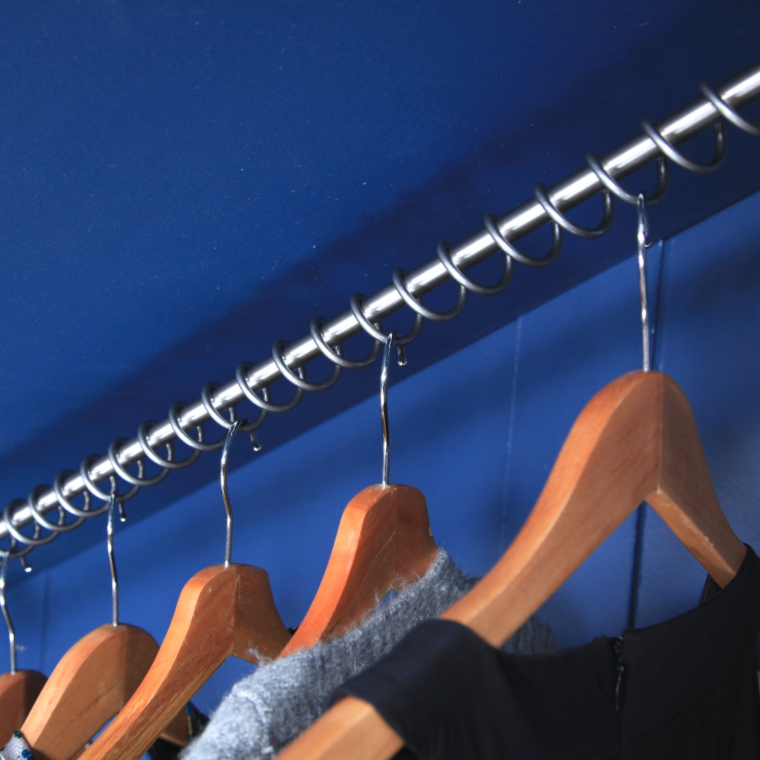 Internal of a sloped ceiling wardrobe, painted blue with Zebedee Any angle hanging rail, Wooden hangers and clothes