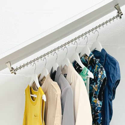 Internals of an eaves fitted wardrobe with clothing items hanging on a zebedee sloping clothes rail against a white background
