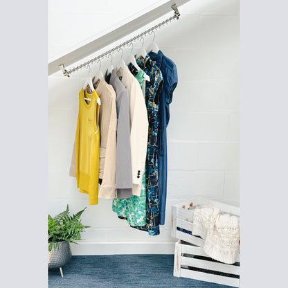 Clothing hanging on a zebedee hanging rail set in a loft angled open wardrobe with a white wall and plant in the background