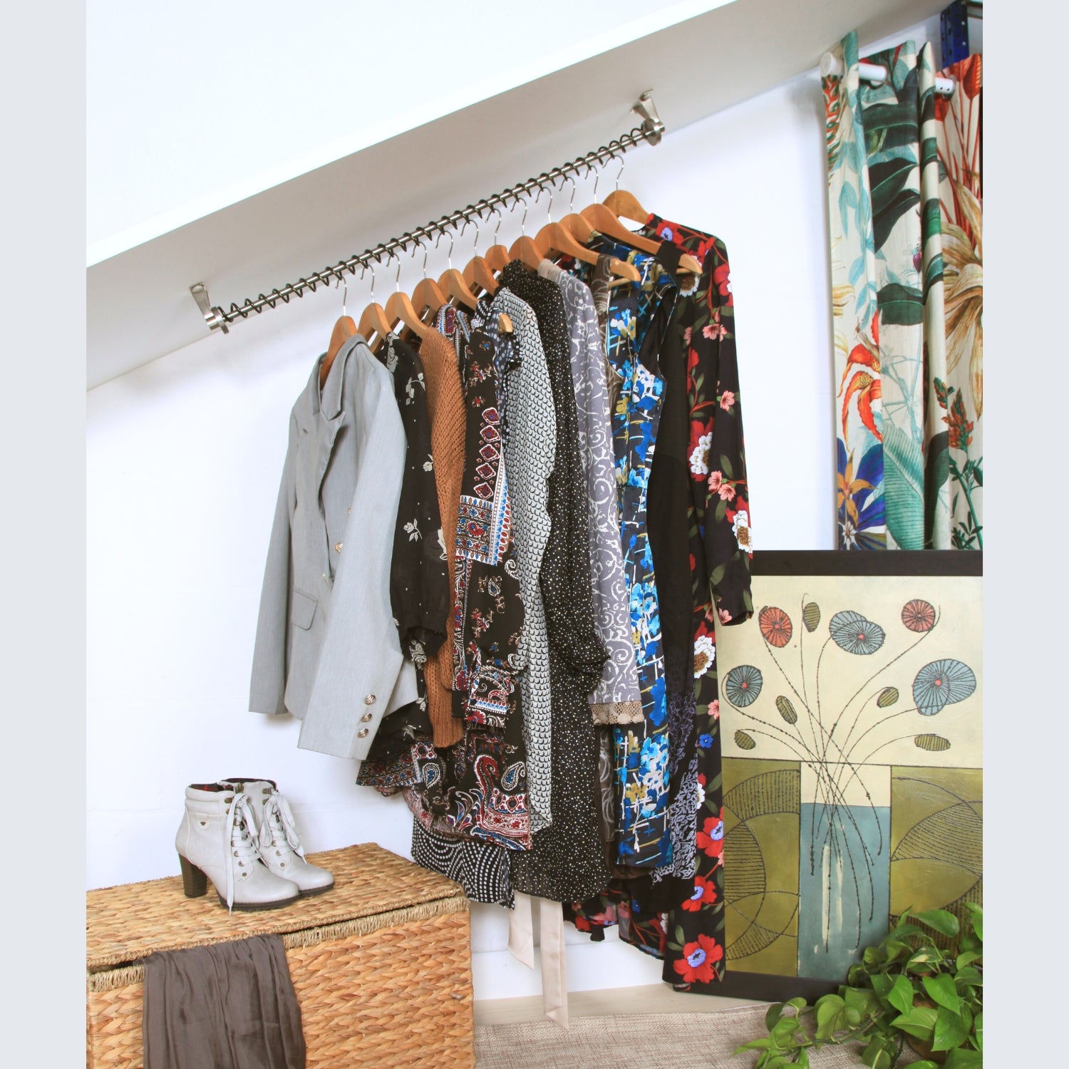 Zebedee Angled clothing rack with various garments fitted to a coombed ceiling, against a white wall, with a plant and woven basket in the foreground.