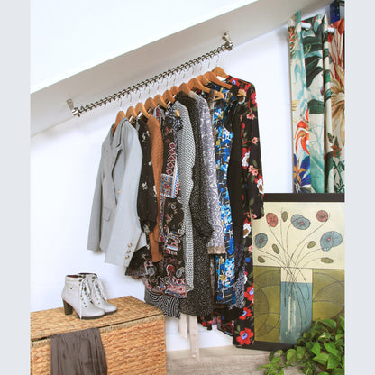 Zebedee Angled clothing rack with various garments fitted to a coombed ceiling, against a white wall, with a plant and woven basket in the foreground.