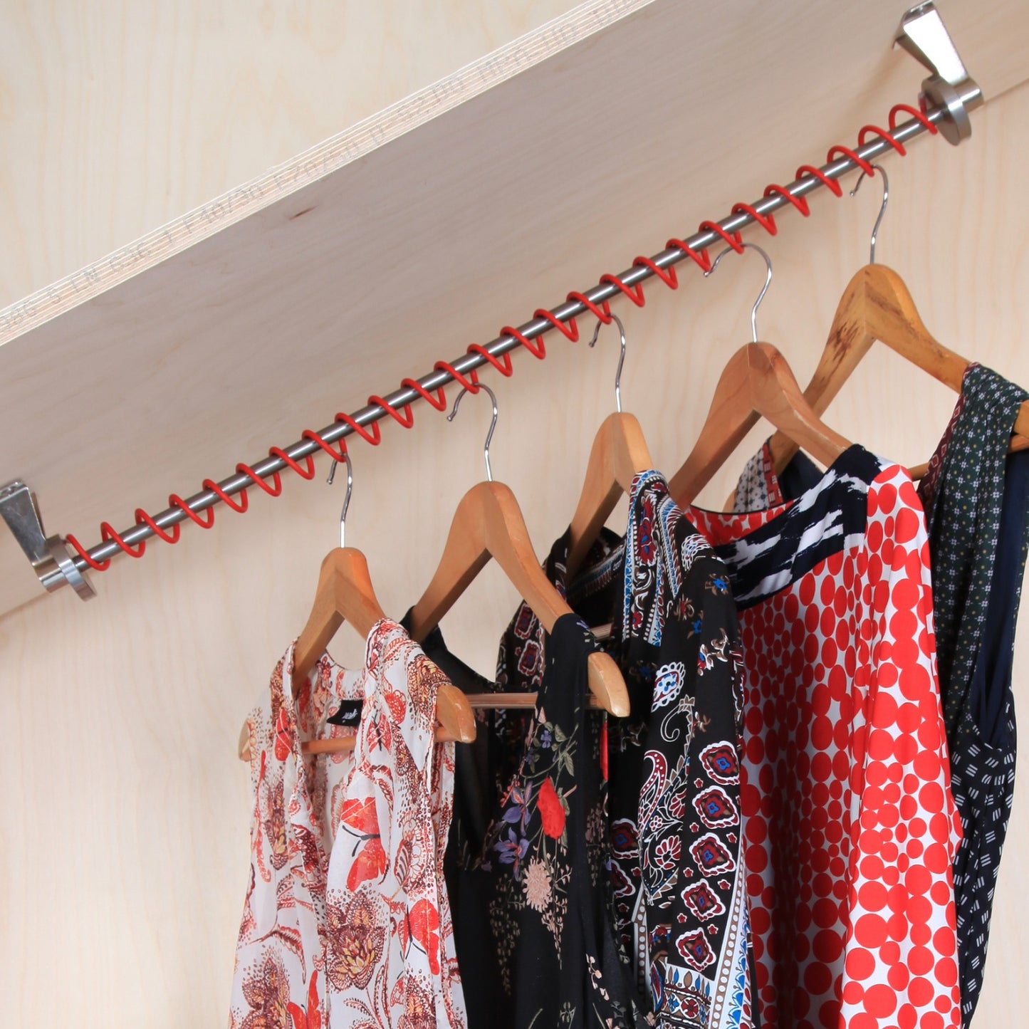 Clothing items on wooden hangers hanging on a Zebedee red under stairs clothes rail in a  wood panelled under stairs area. 