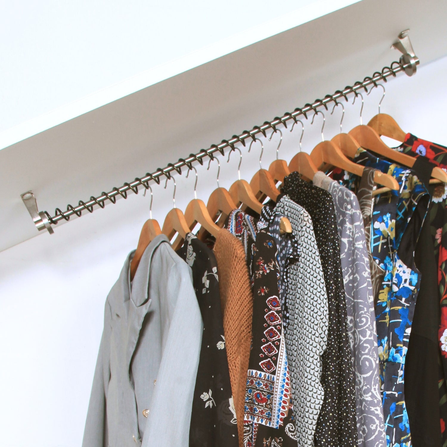 Angled wardrobe rail rack fitted to a coombed ceiling with various garments hanging on it against a white background
