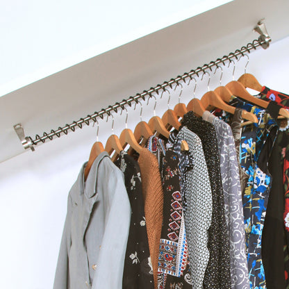 Angled wardrobe rail rack fitted to a coombed ceiling with various garments hanging on it against a white background