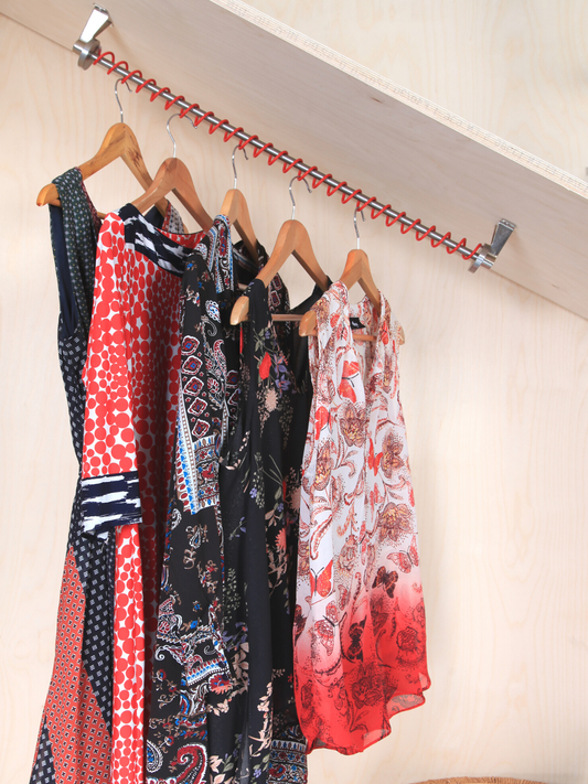 Zebedee red under stairs clothes rail  top mounted with clothes on hangers, following the angle of the ceiling. 