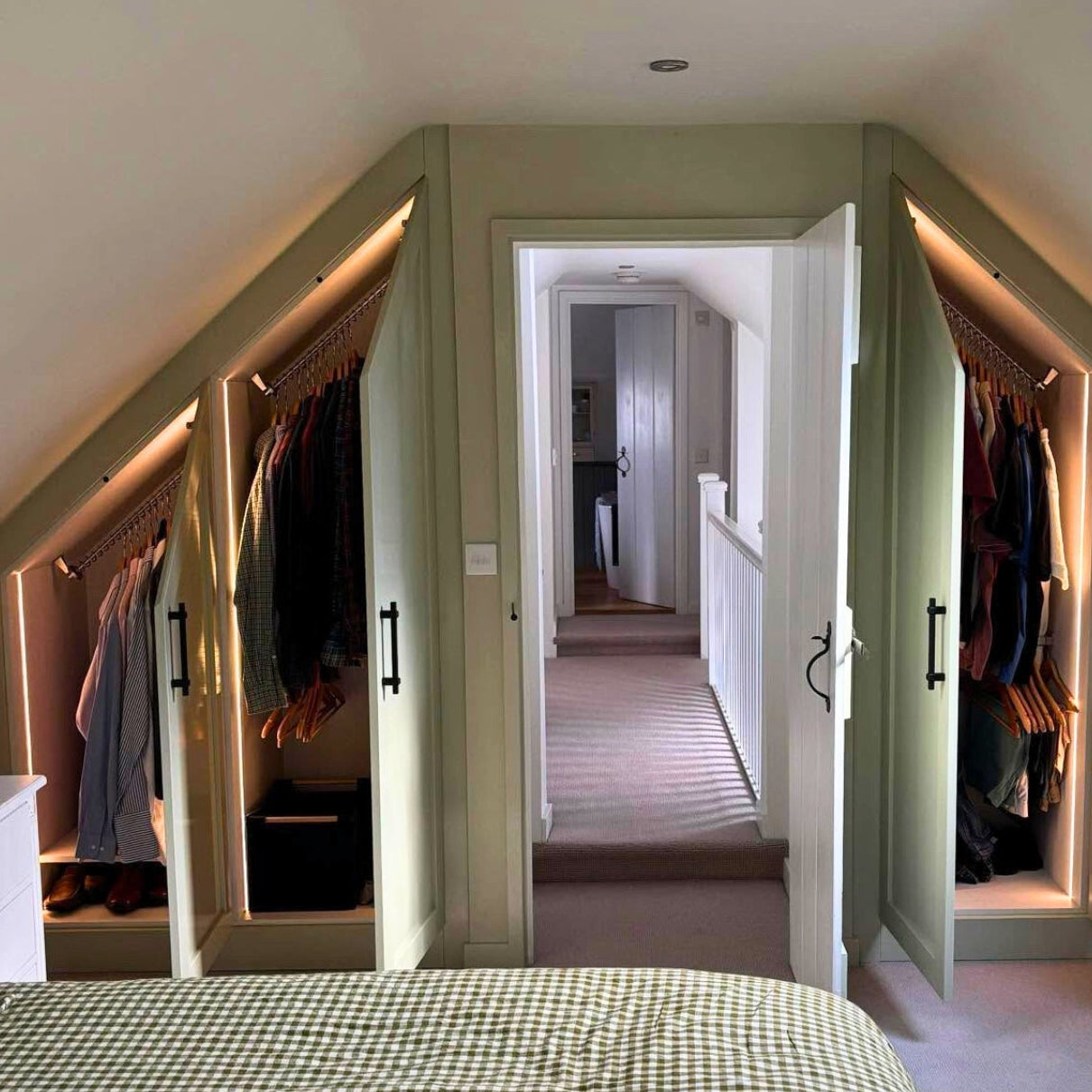 Attic bedroom with sloped ceiling fitted wardrobes, doors open revealing Zebedee's space saving sloped ceiling clothes rails, illuminated by recessed lights.
