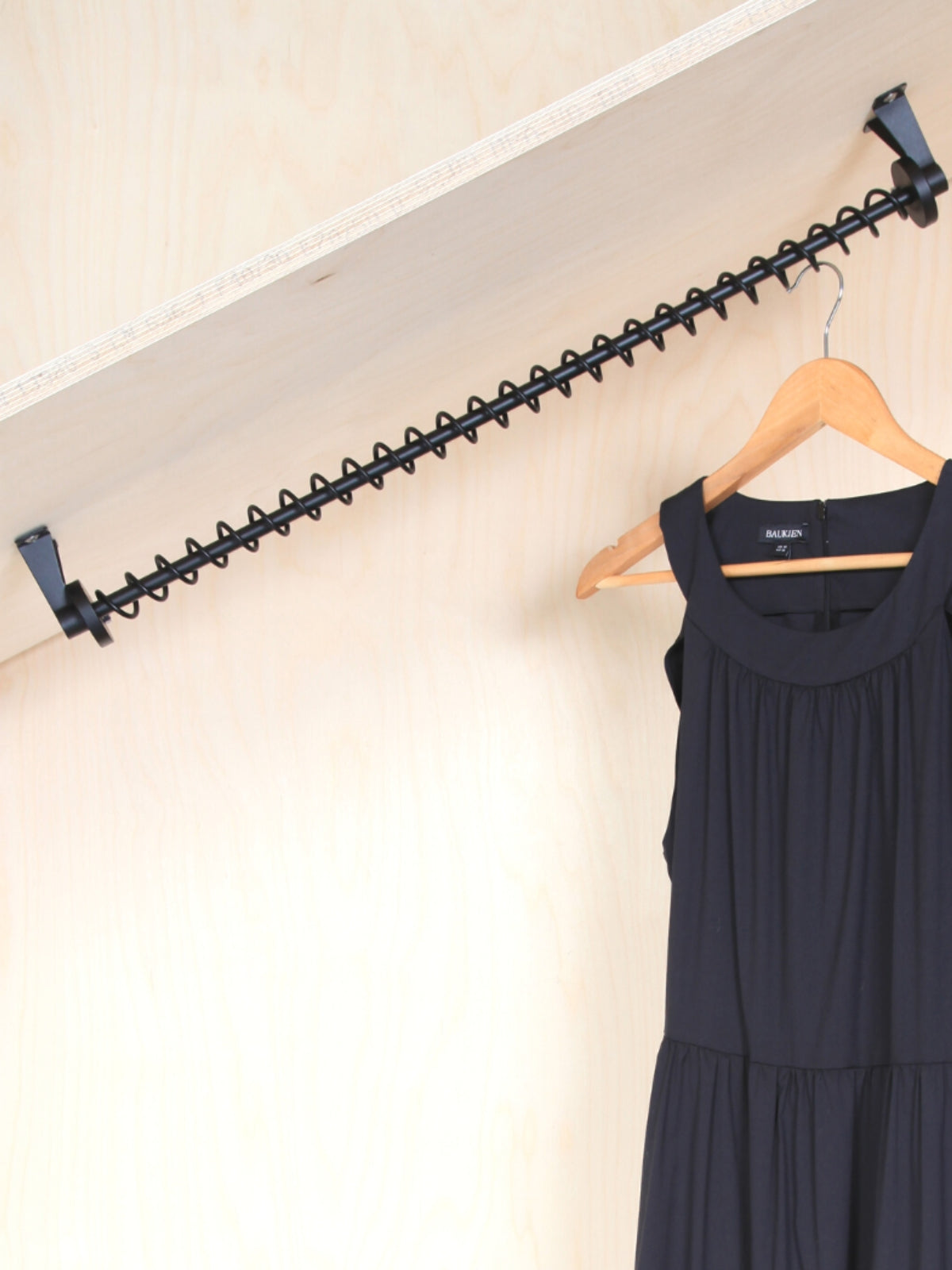 Black sloping clothes rack top mounted on a wall with a black dress hanging from it.
