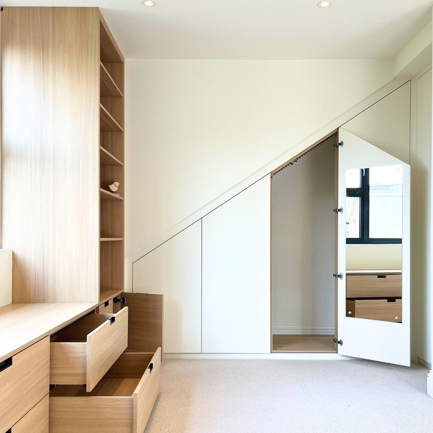 Modern attic interior with bespoke angled wooden cabinetry, sloping hanging rails, mirror and drawers