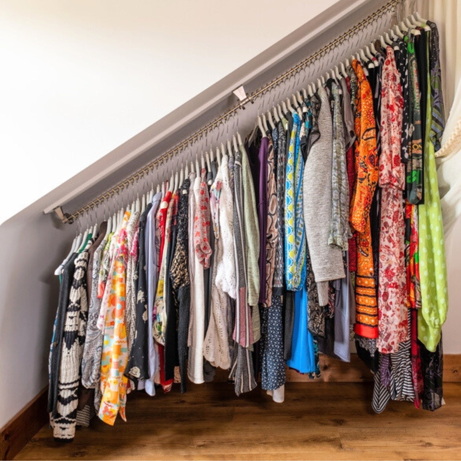 Sloping Clothing rack with a variety of colorful clothes hanging on it against a white wall.