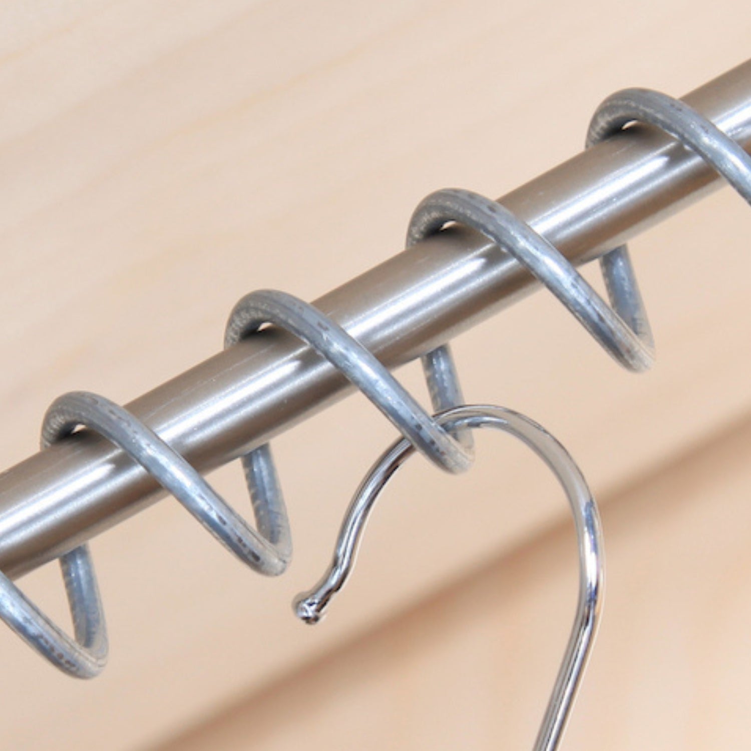 Close up of Zebedee hanging rail stainless steel rod and coil on a beige background