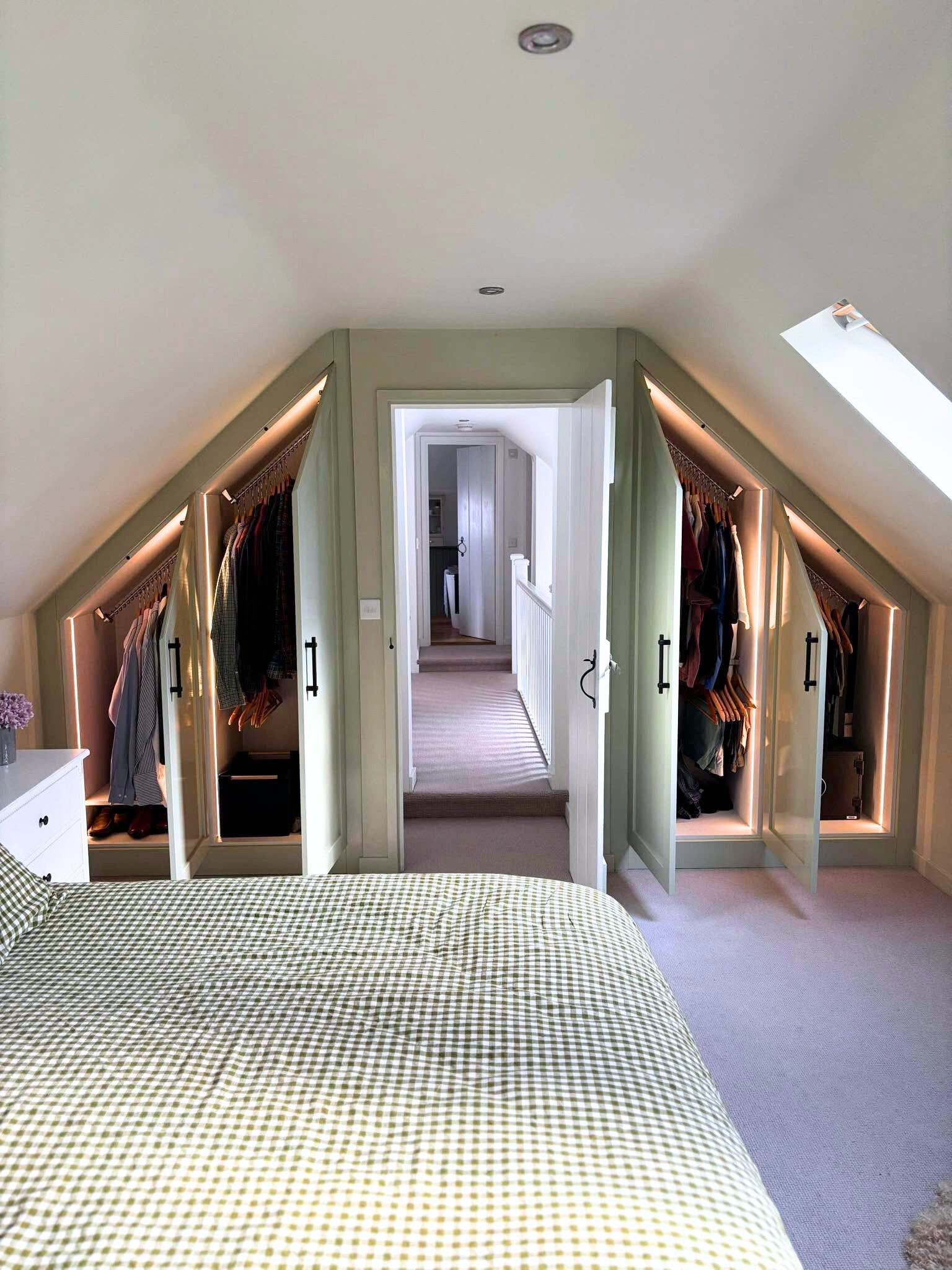 Attic bedroom with built-in angled wardrobes, sloping clothes rails providing full-length hanging, and skylight